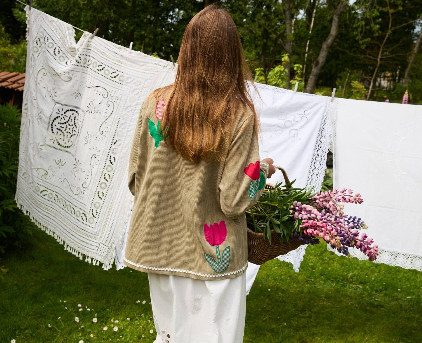 Person wearing a beige cardigan with floral embroidery, holding a bouquet of flowers outdoors.